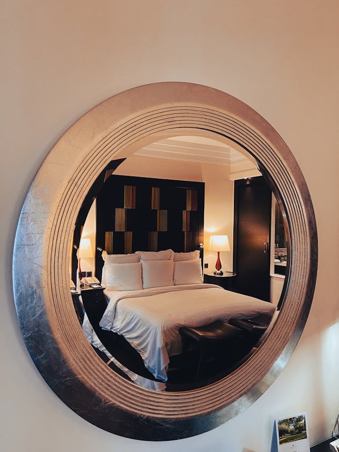 A luxurious hotel bedroom captured through a stylish circular wall mirror for interior design inspiration.